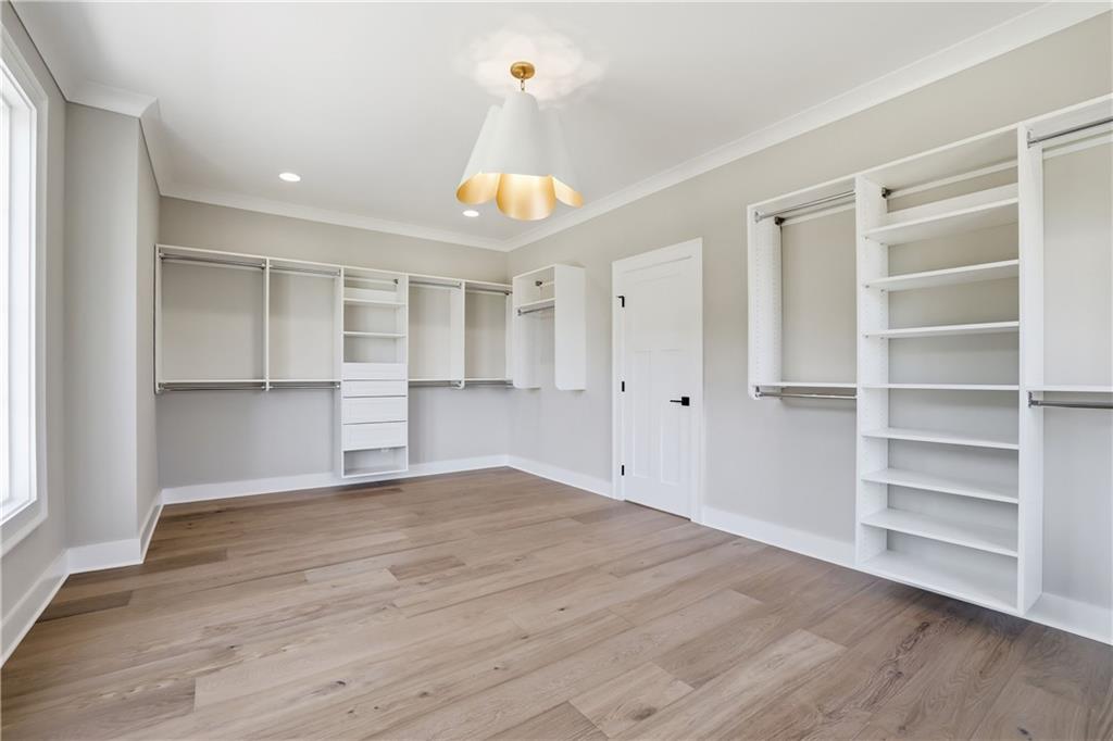 Walk-in closet with white built-in shelving and drawers, hanging rods, and wide-plank wood flooring.