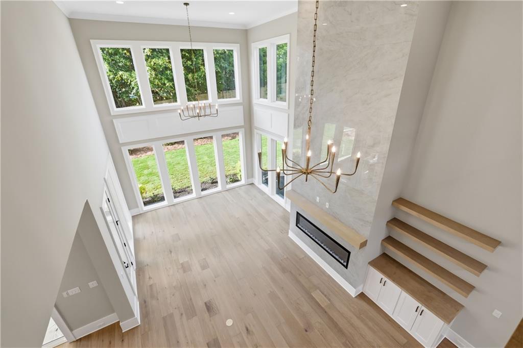 Two-story living room with a marble fireplace, tall windows, and pale wood floors.