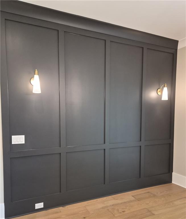 Dark paneled feature wall with two brass sconces above light wood flooring.