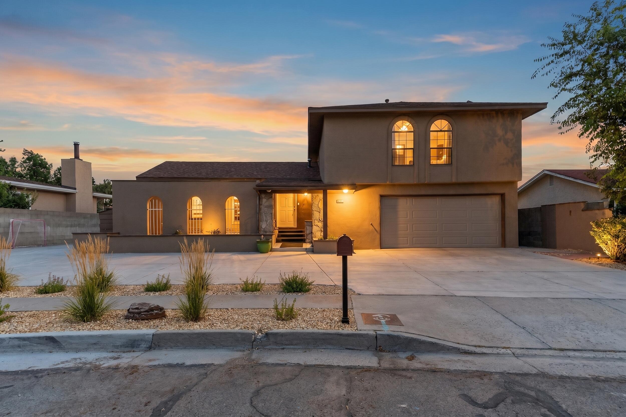 Two-story stucco home with glowing arched windows and a lit entry at dusk.