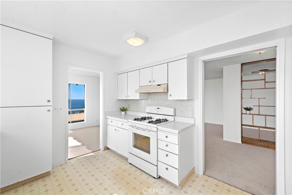 White kitchen with a gas range and patterned floor, with an ocean view through the doorway.