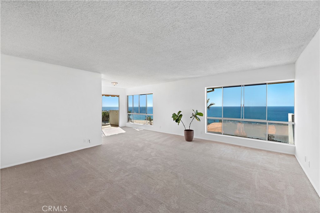 Empty carpeted living room with large windows overlooking the ocean.