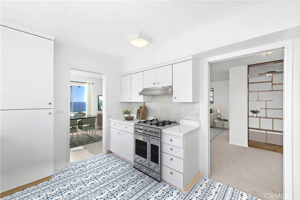 White kitchen with a stainless gas range, patterned tile floor, and ocean visible through the adjoining dining room.