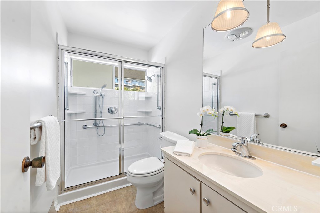 Bathroom with a glass-enclosed shower and cream vanity topped with white orchids.