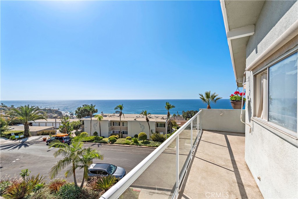 Balcony overlooking the ocean, with a glass railing and coastal neighborhood below.