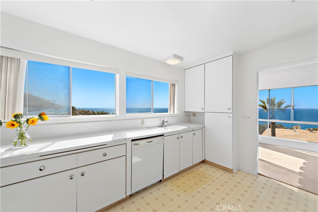 White kitchen with wide ocean-view windows and a doorway opening to a patio.