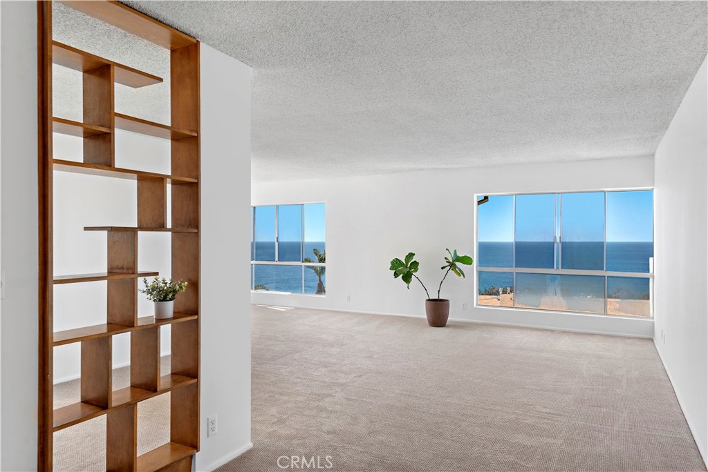 Vacant living room with built-in wood shelving and broad ocean views through large windows.