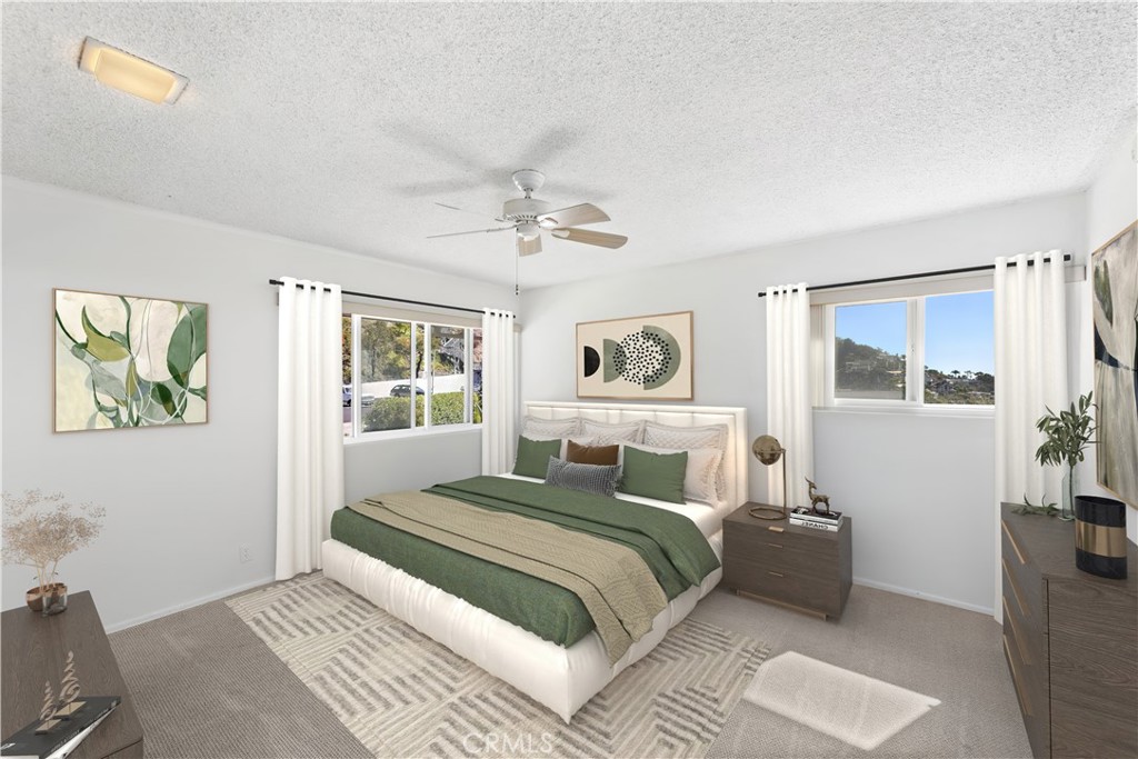 Bedroom with green bedding, a geometric rug, and windows overlooking a hillside.