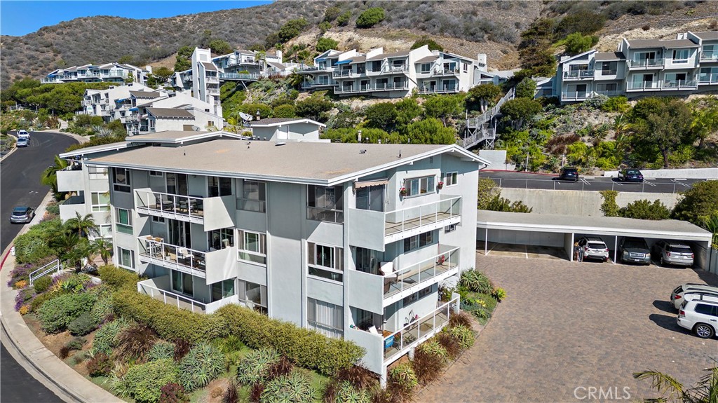 Aerial view of a condominium building with balconies, hillside residences, and parking.