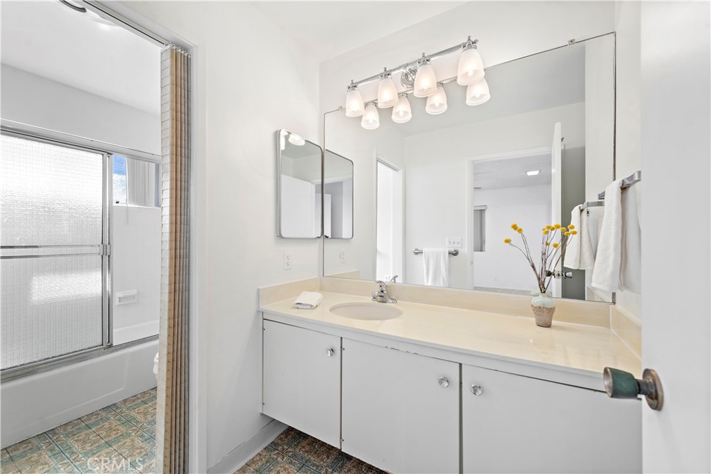 Bathroom with a long white vanity and mirror beside a tub with frosted-glass doors.