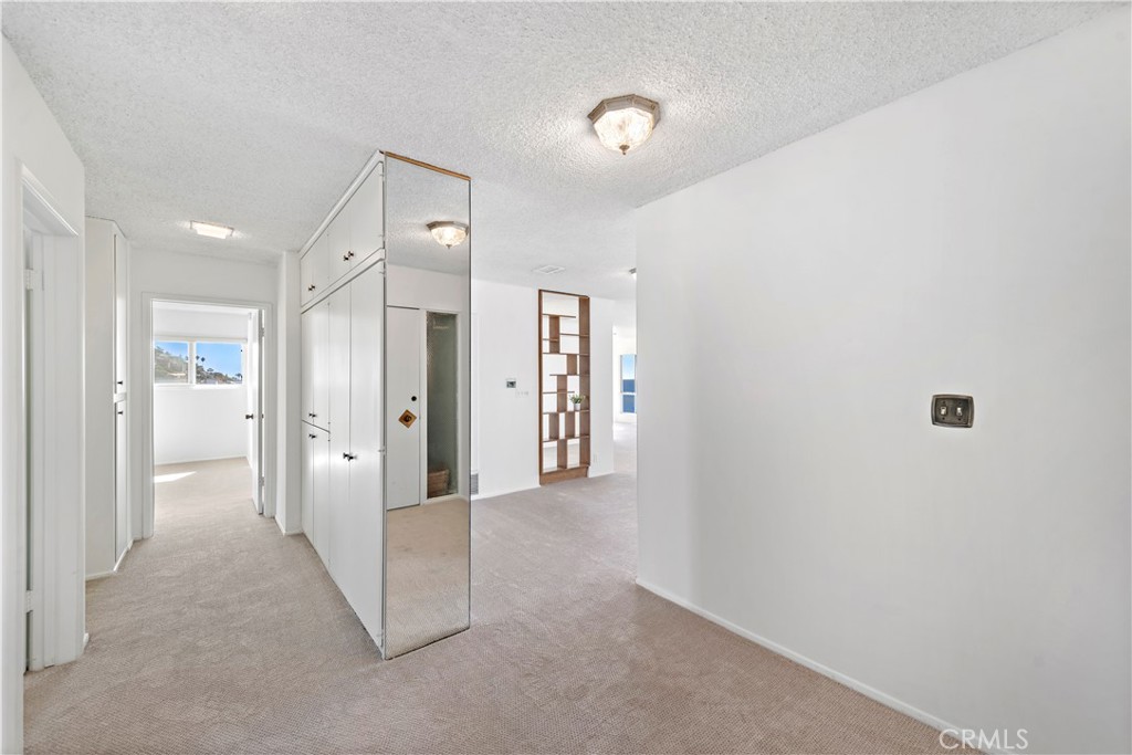 Carpeted condo hallway with mirrored closet doors and open doorways to bright rooms.