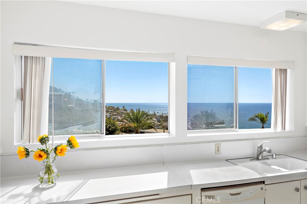 Bright kitchen with sunflowers on the counter and ocean views through two windows.