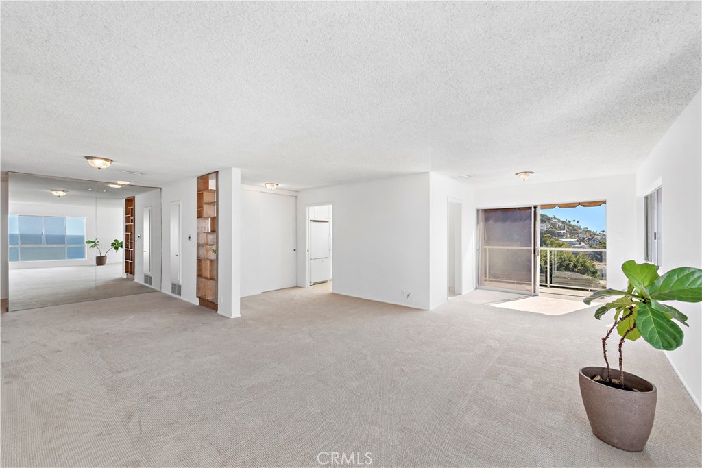 Unfurnished living room with beige carpeting, a balcony, and a glimpse of ocean in the mirror.