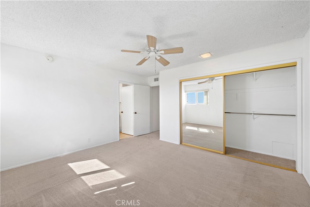 Empty carpeted bedroom with a ceiling fan and mirrored sliding closet doors.