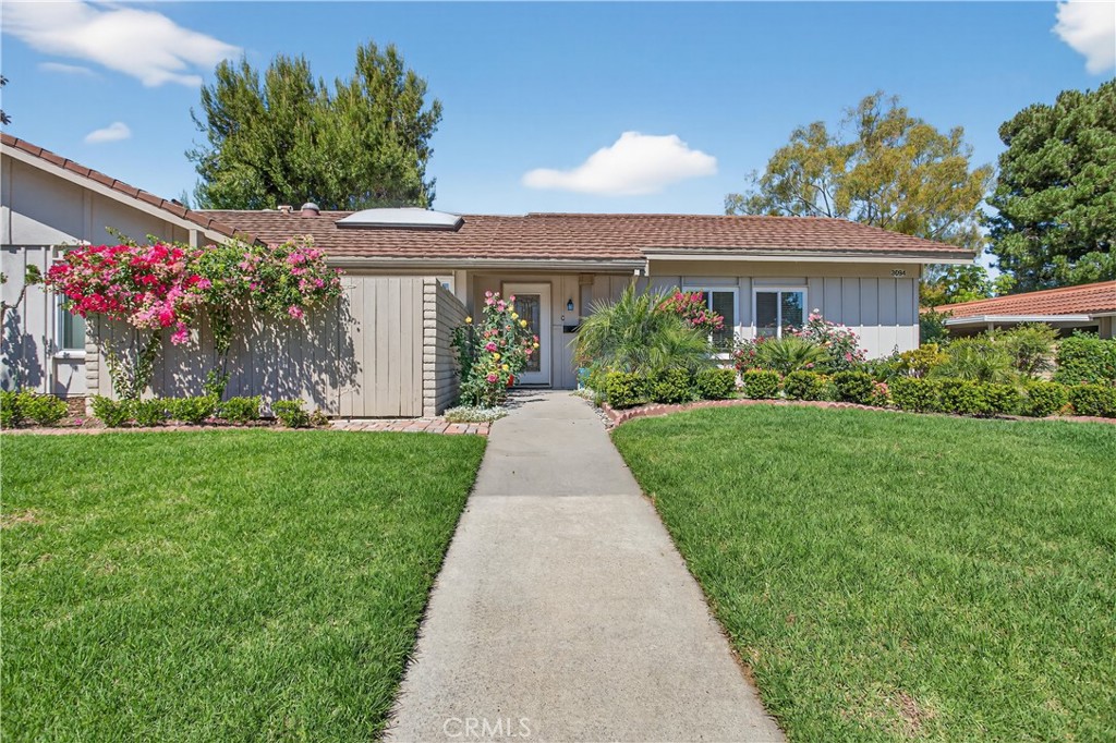 Single-story home with a walkway through a green lawn and flowering shrubs along the facade.