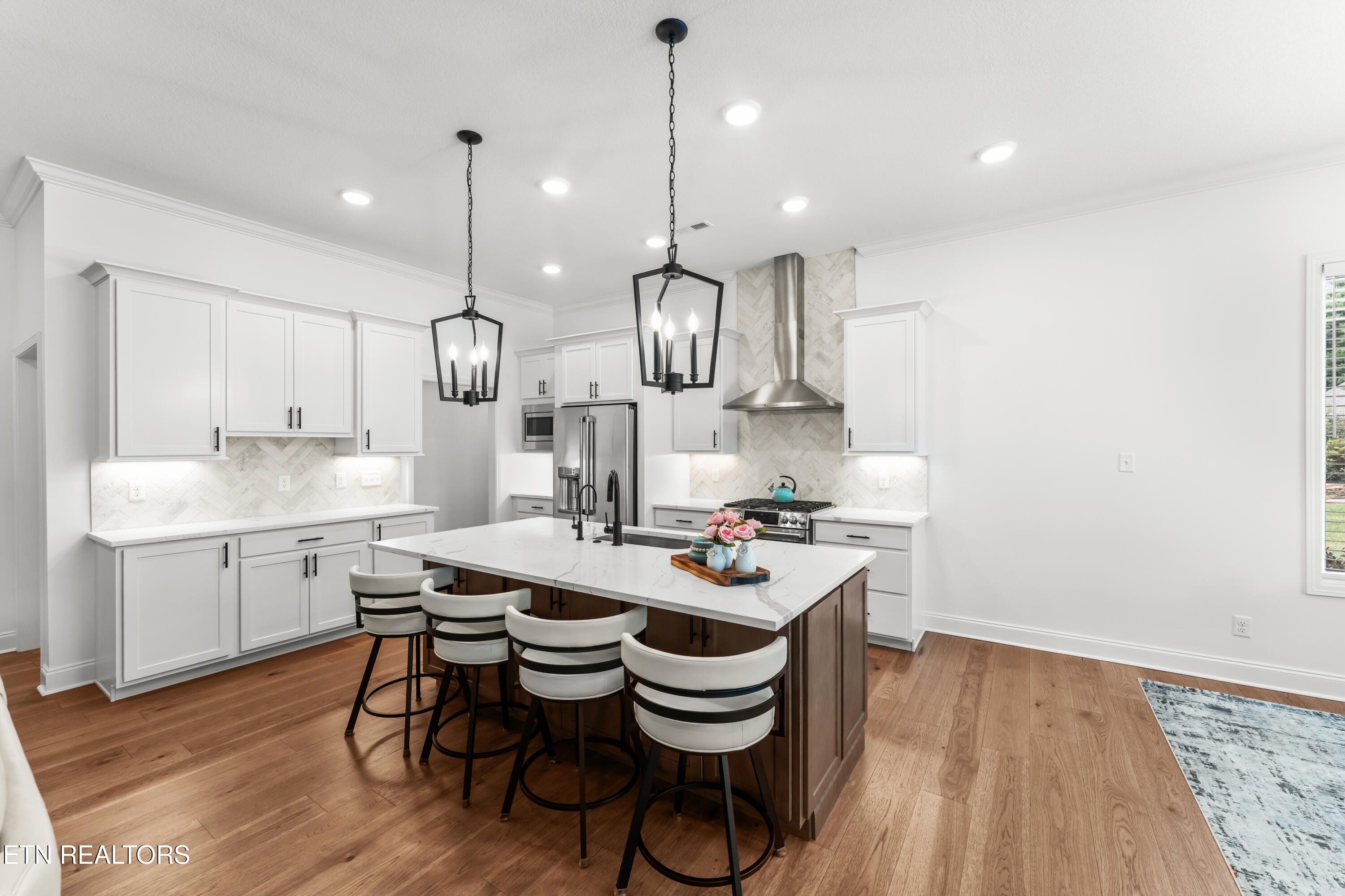Kitchen with white cabinets, stainless appliances, and a large island with four bar stools.