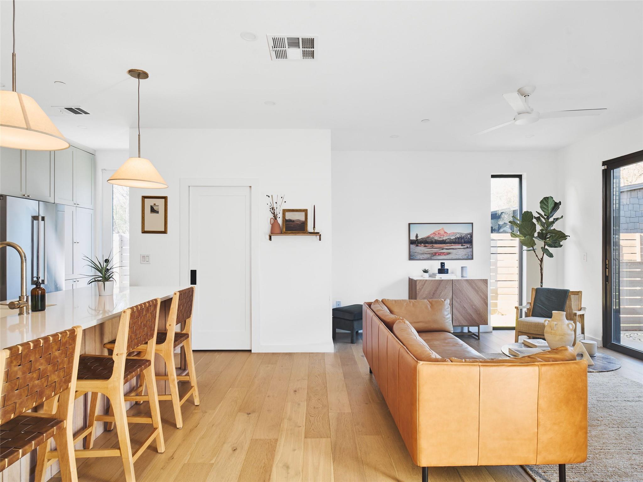 Open-plan living room and kitchen with a tan leather sectional and woven dining chairs.