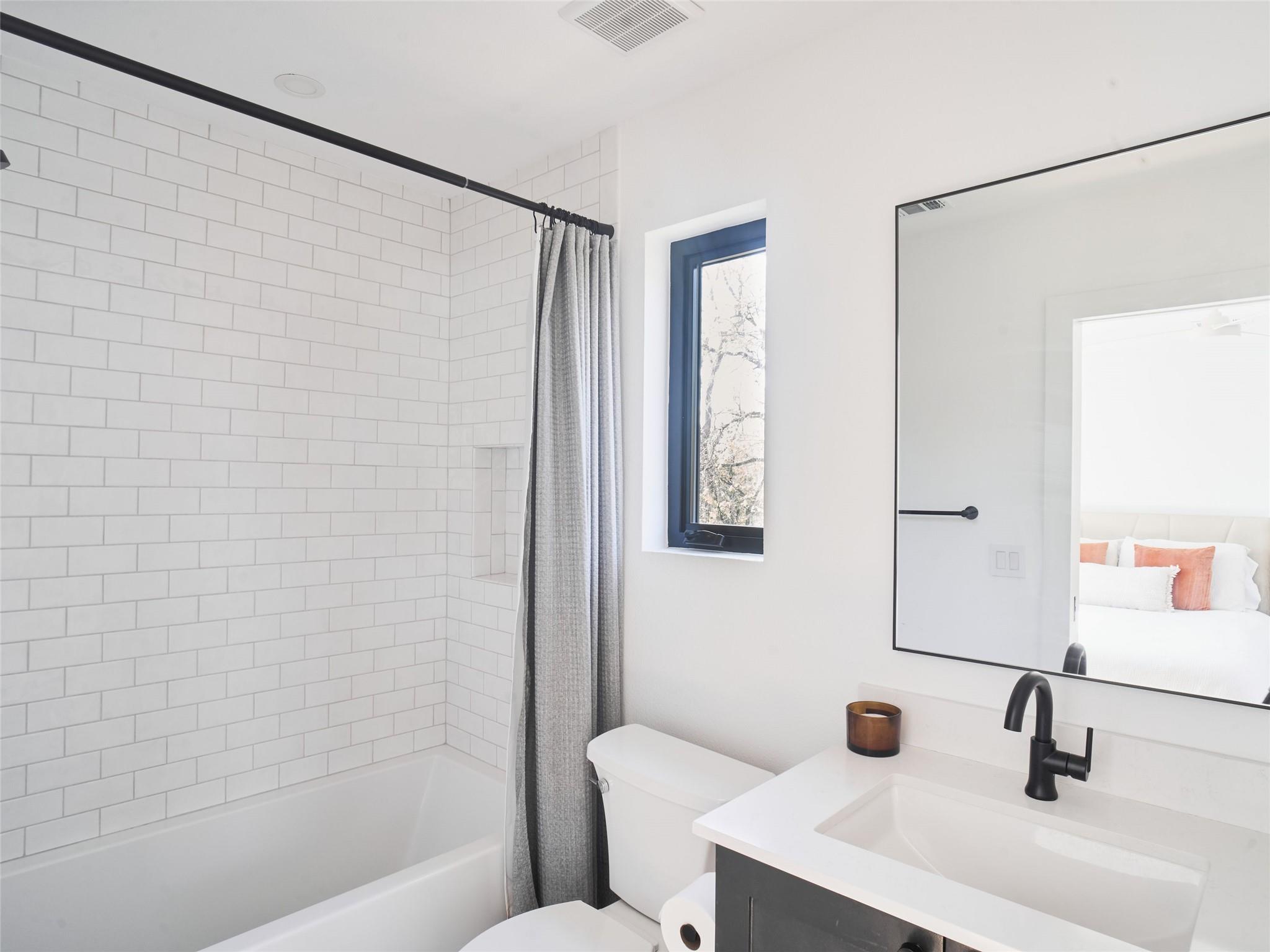 Bright bathroom with white subway tile, a bathtub, gray shower curtain, and black vanity faucet.