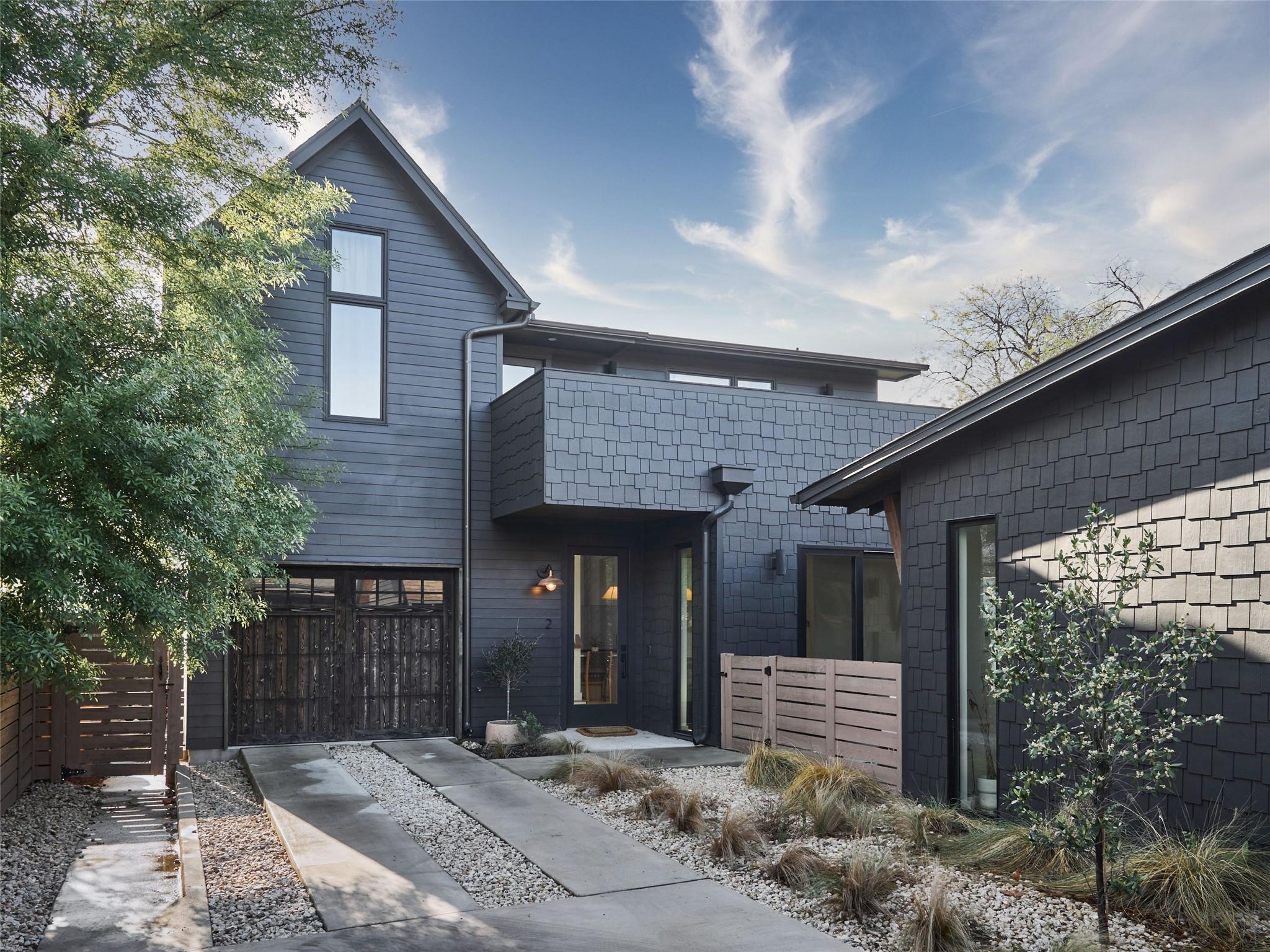 Modern dark-gray home with shingle siding, a gabled roof, and a concrete path through gravel landscaping.