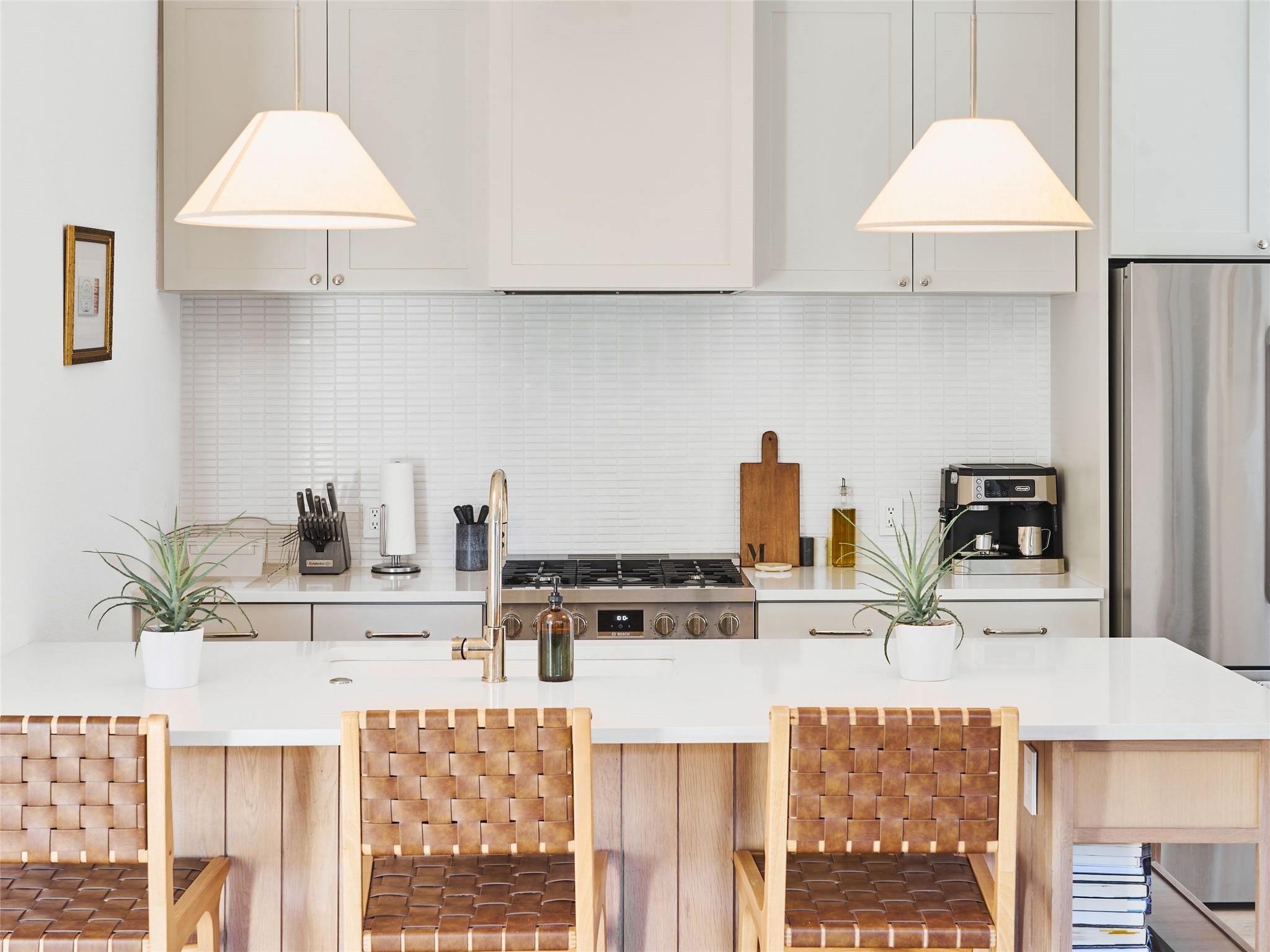 Bright kitchen with white cabinets, stainless appliances, and a large island lined with woven leather chairs.