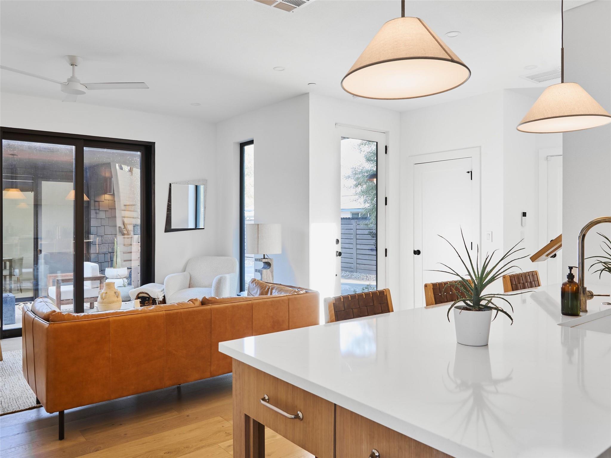 Open-plan living room and kitchen with a white island, caramel leather sofa, and black-framed patio doors.
