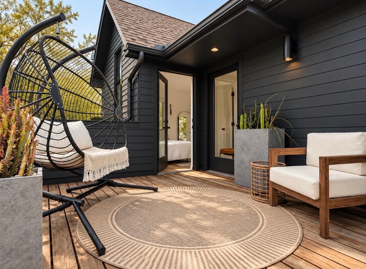 Furnished deck patio with a hanging swing chair, white seating, potted plants, and a round rug.