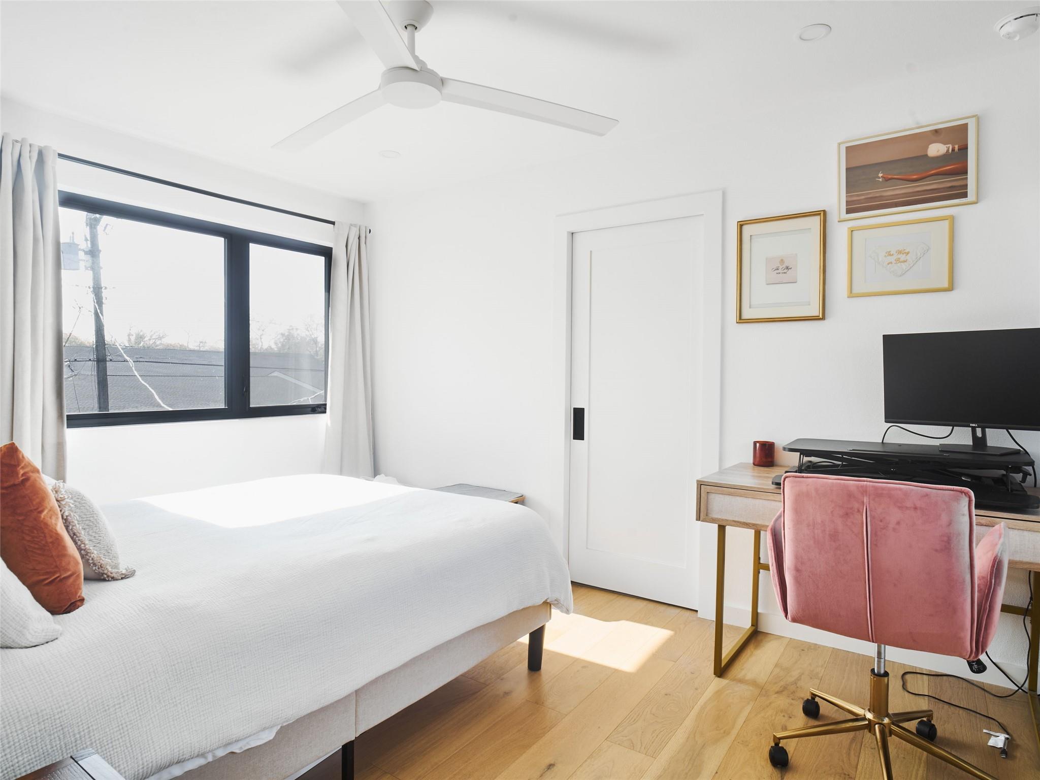 Bedroom with a white bed, black-framed window, and desk with a pink chair.