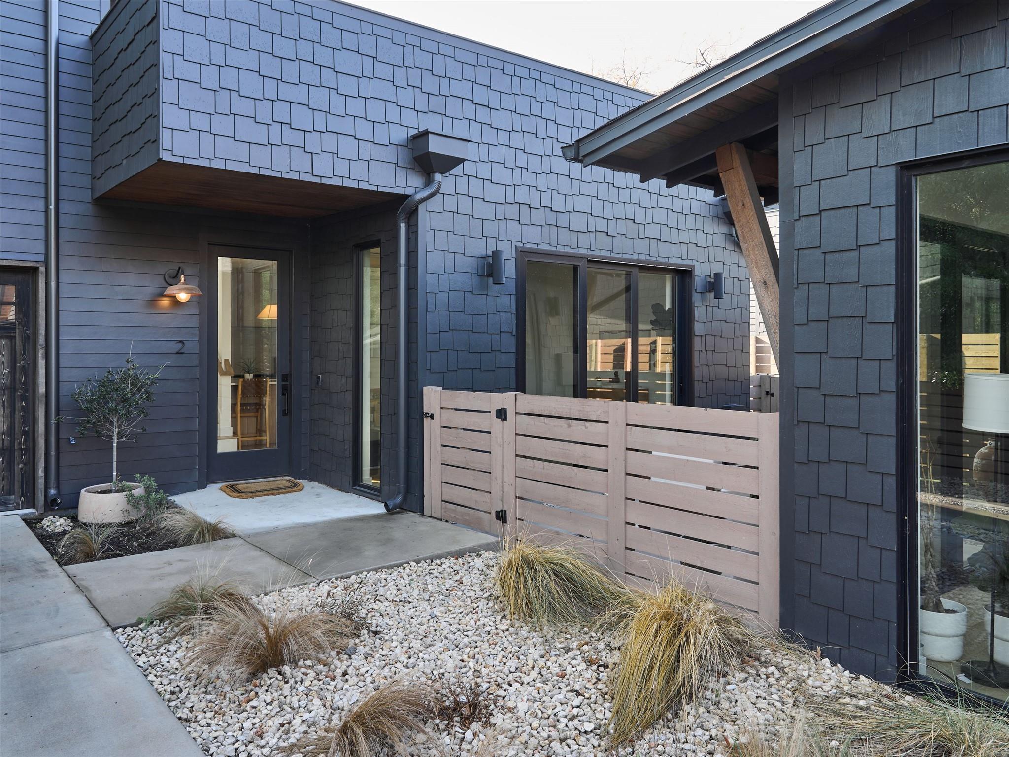 Modern home entrance with dark blue shingles, a glass-paneled door, and pale wood privacy fence.