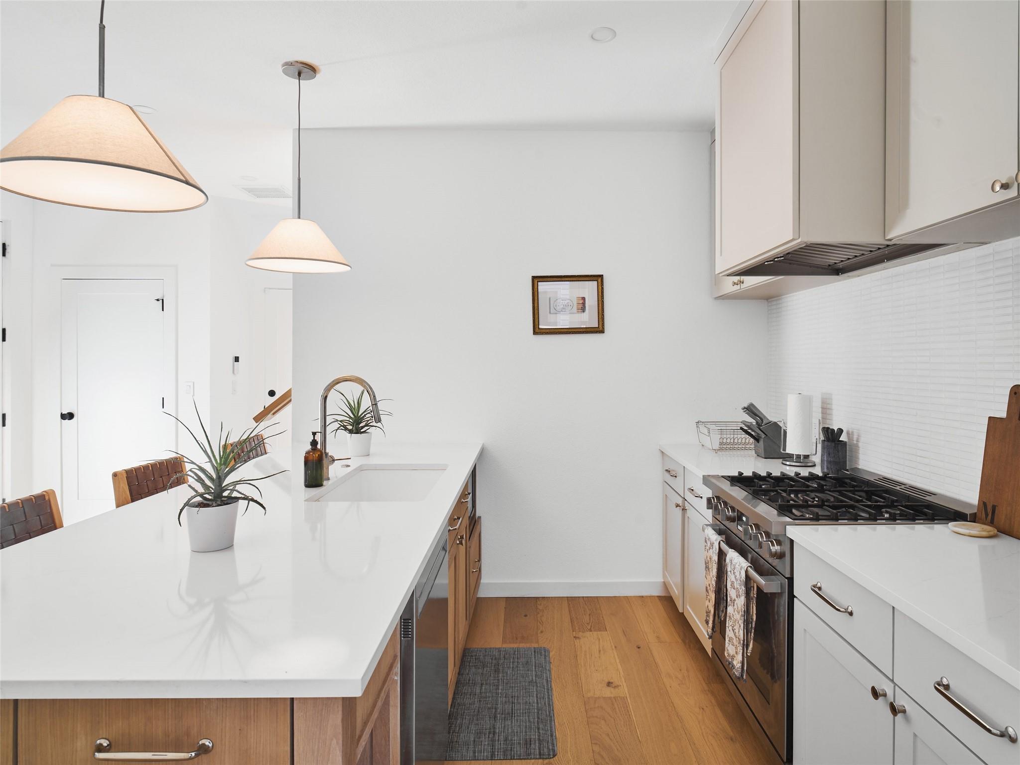 Modern kitchen with a large white island, pendant lights, and stainless steel gas range.