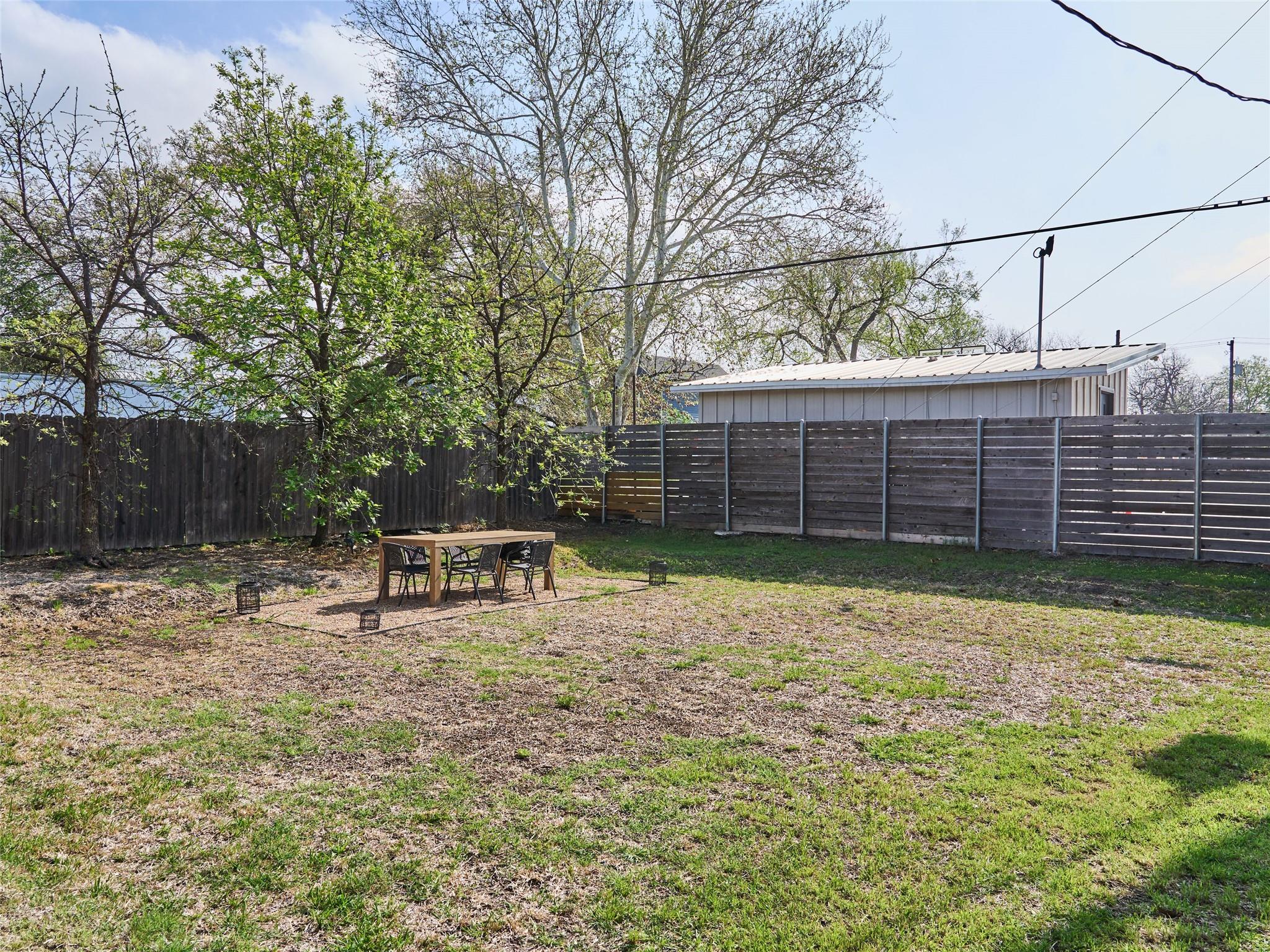 Fenced backyard with mature trees and a patio dining table and chairs.