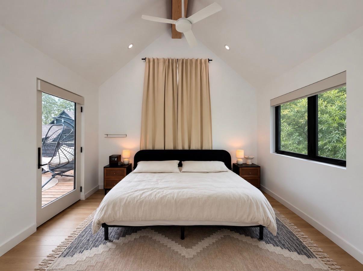 Bedroom with a white bed beneath a vaulted ceiling, opening onto a deck through a glass door.