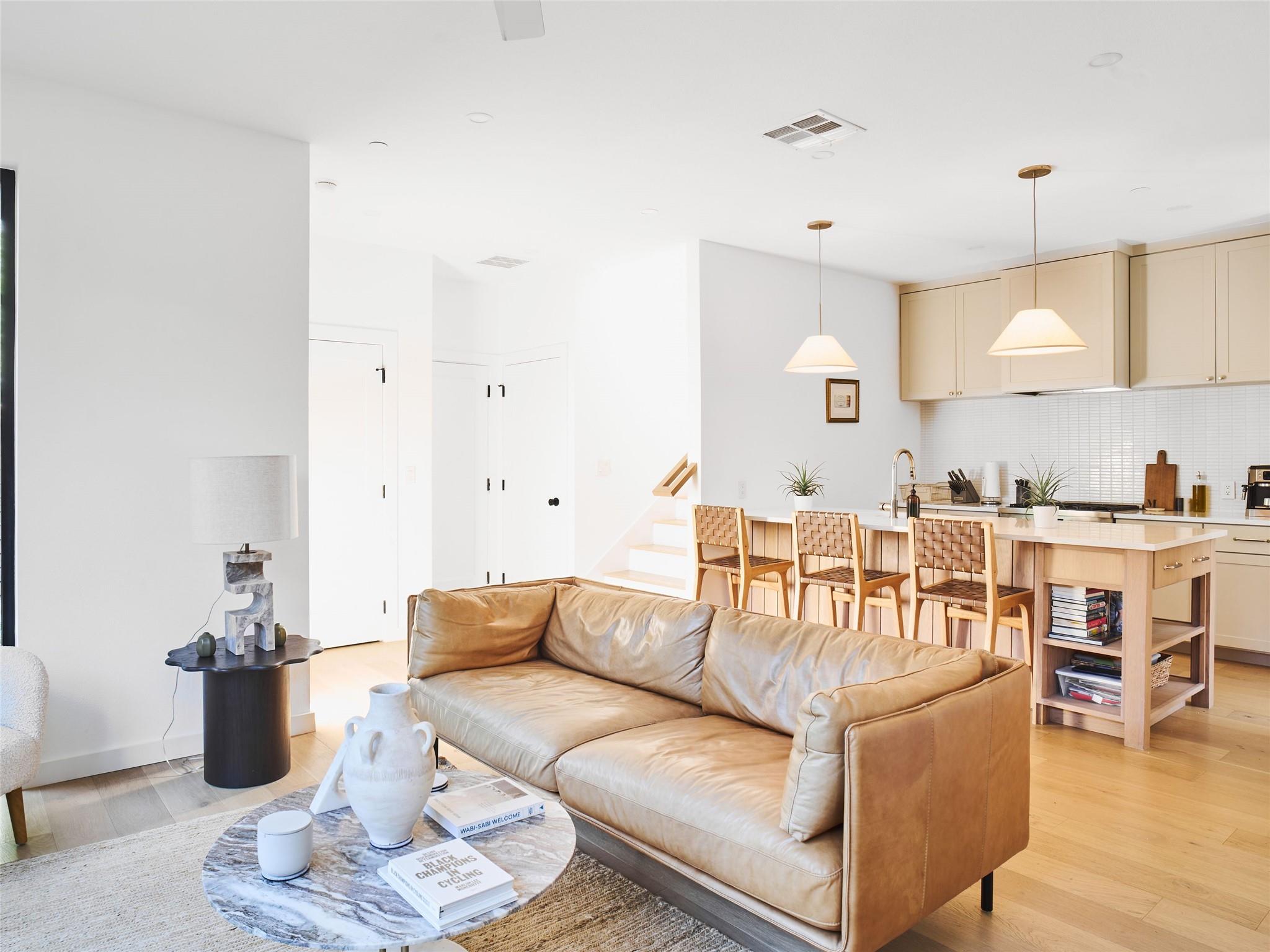 Open-plan living room with a tan leather sofa facing a light wood kitchen island.