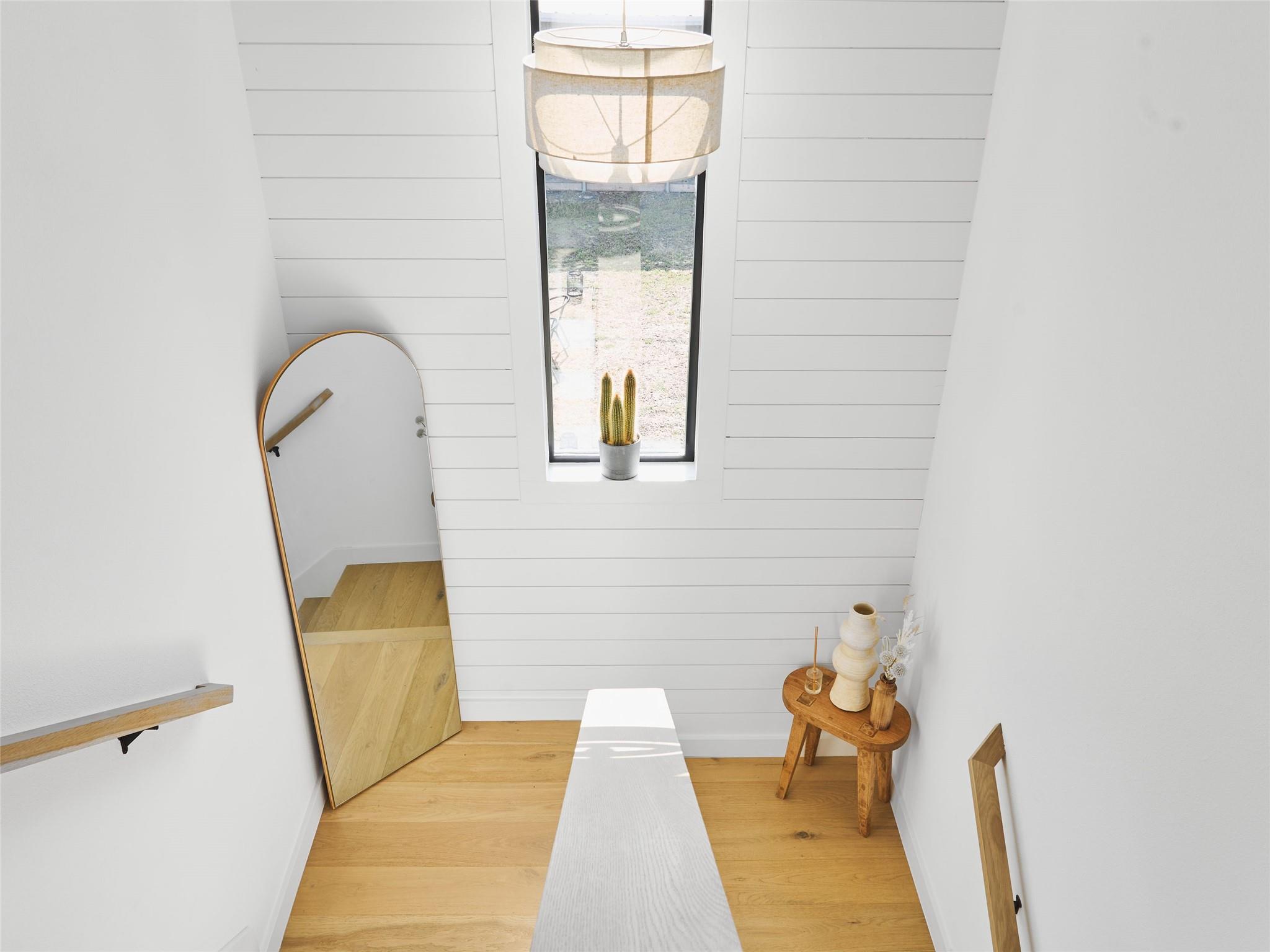 Bright landing with a tall window, arched mirror, long bench, and light wood floor.