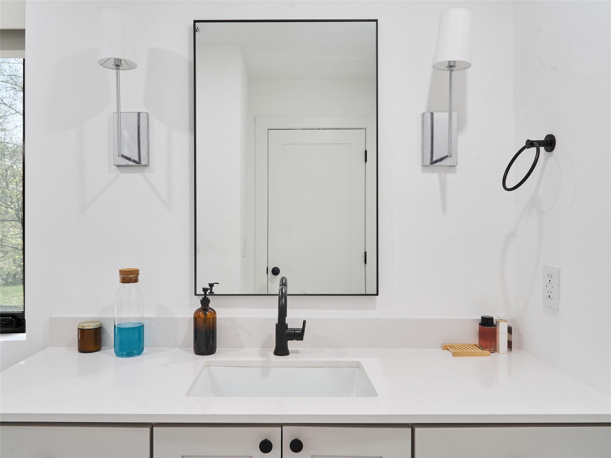 Bathroom vanity with a black faucet, white sink, large mirror, and matching wall sconces.