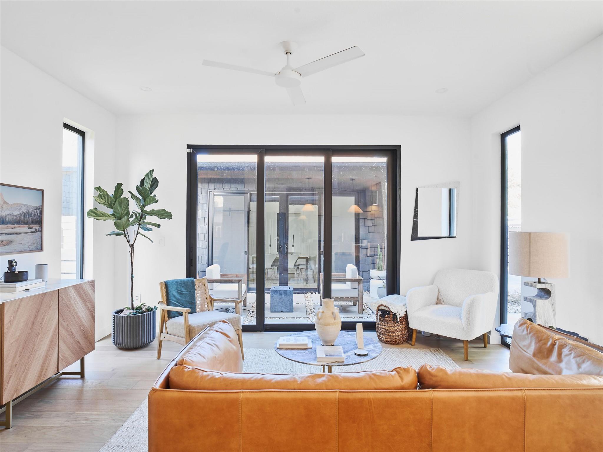 Furnished living room with a caramel leather sofa, white armchair, and glass doors to a courtyard.