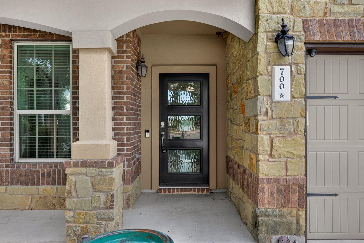 Stone-and-brick home entry with a black glass-panel door and address plaque 700.