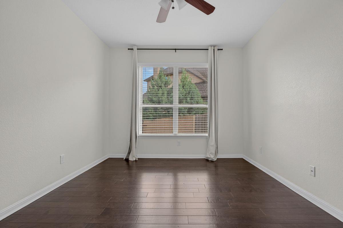 Empty bedroom with dark hardwood floors, a ceiling fan, and a large curtained window.
