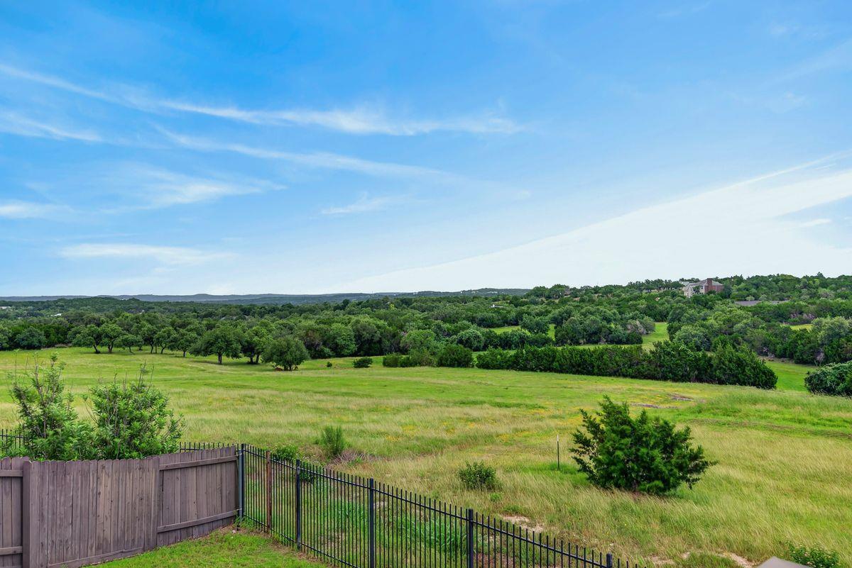 Green meadow and tree-covered hills viewed over a black metal and wooden fence.