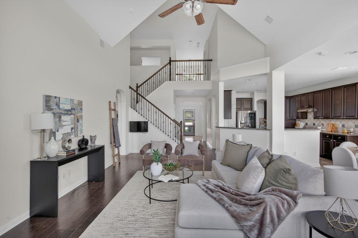 Open-plan living room with vaulted ceiling, staircase, dark wood floors, and adjoining kitchen.