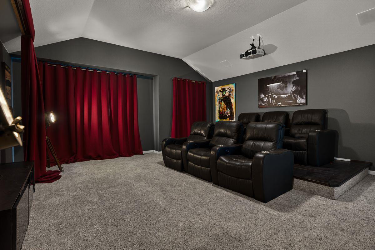 Home theater with raised leather recliners, red curtains, and a ceiling-mounted projector.