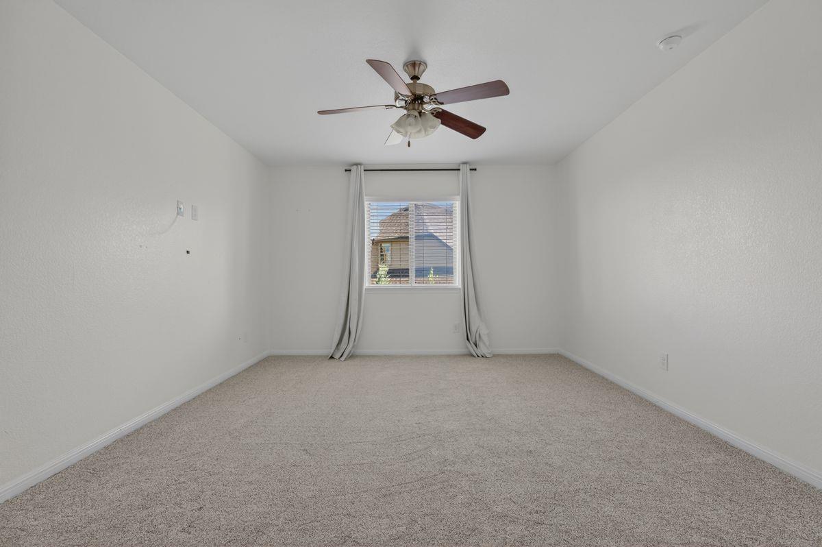 Empty carpeted bedroom with a ceiling fan and curtained window.