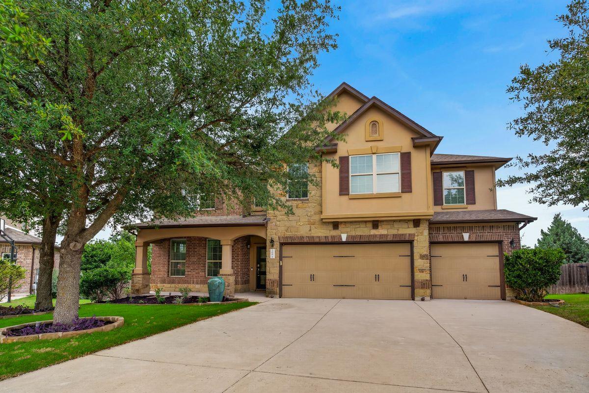 Two-story stone and brick home with a three-car garage and mature trees in front.