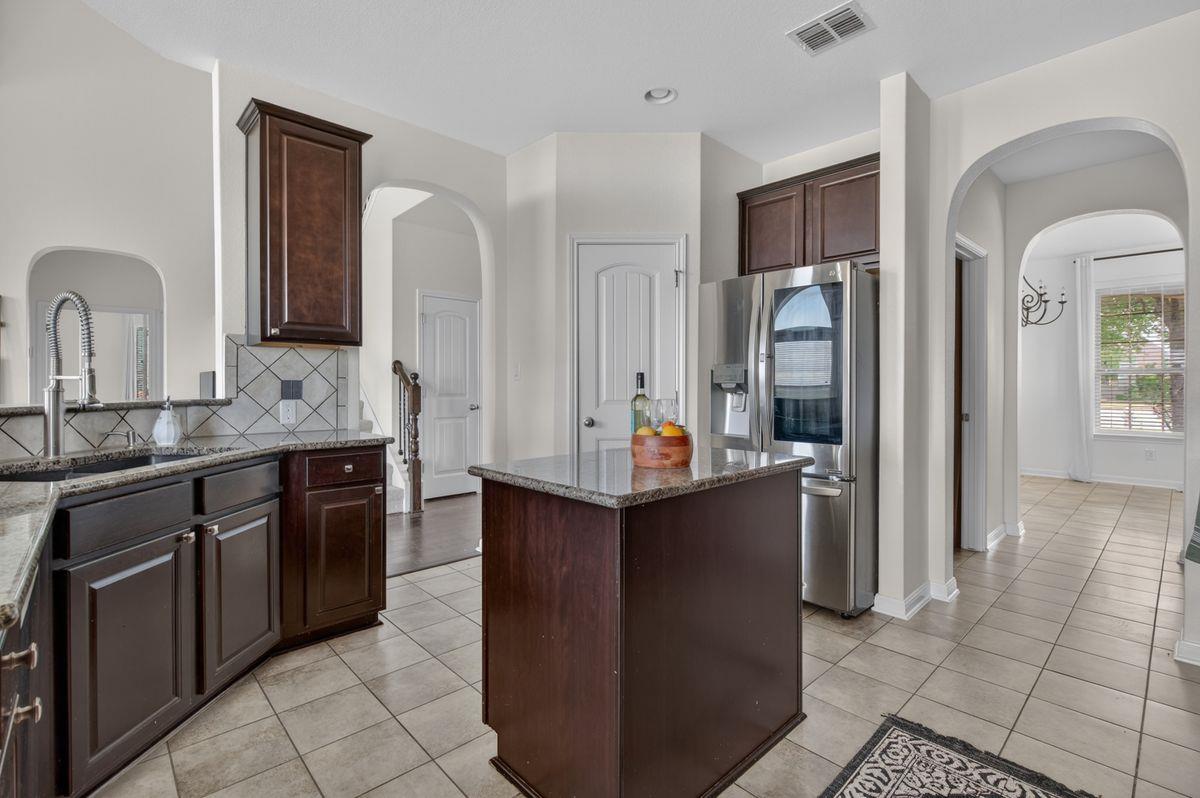 Kitchen with dark wood cabinets, granite counters, stainless steel appliances, and a central island.