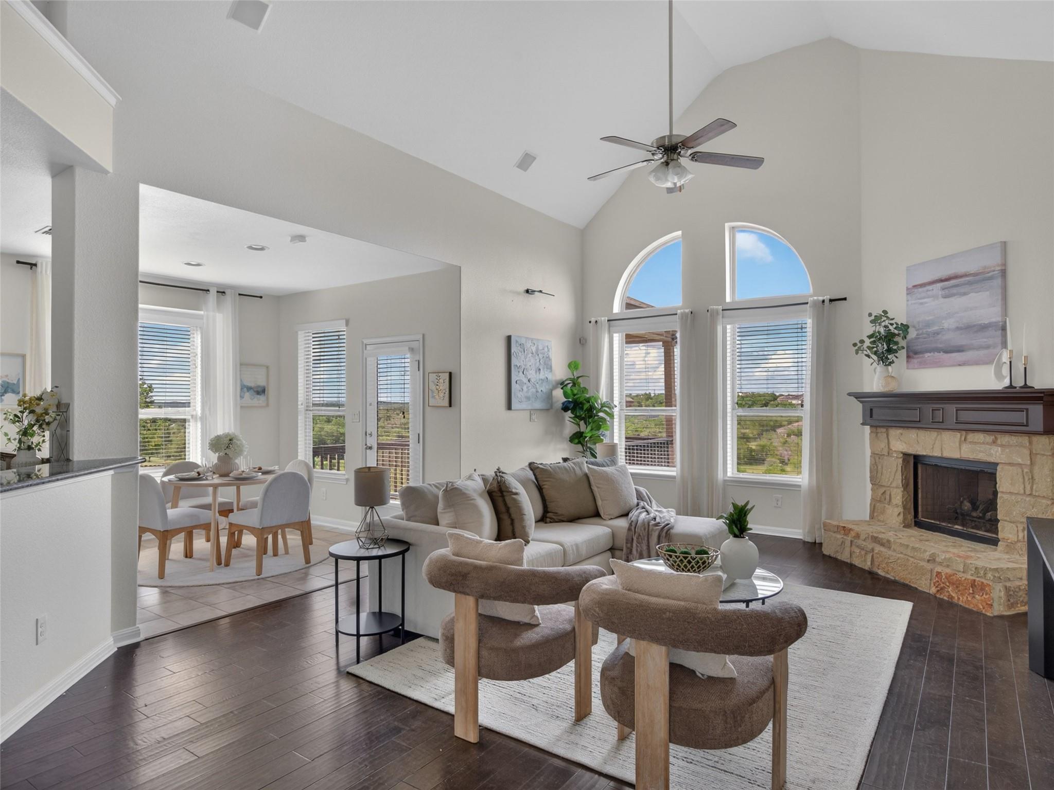 Living room with vaulted ceiling, arched windows, stone fireplace, and adjoining dining area.