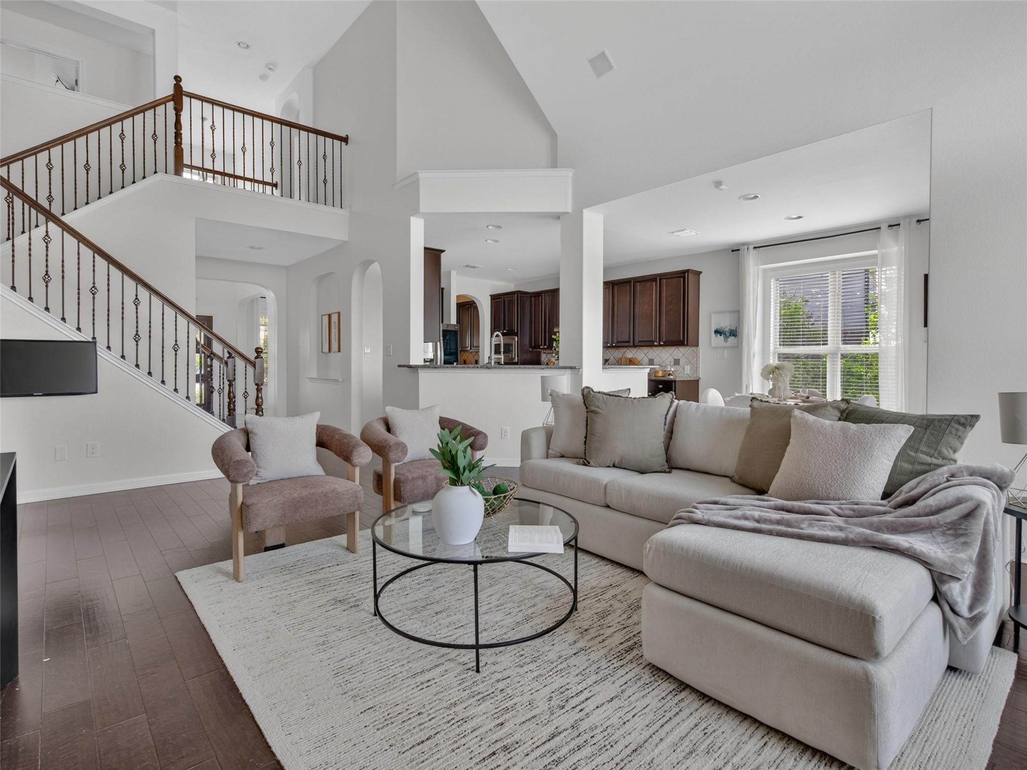 Open-plan living room with a large sectional, dark wood staircase, and kitchen beyond.