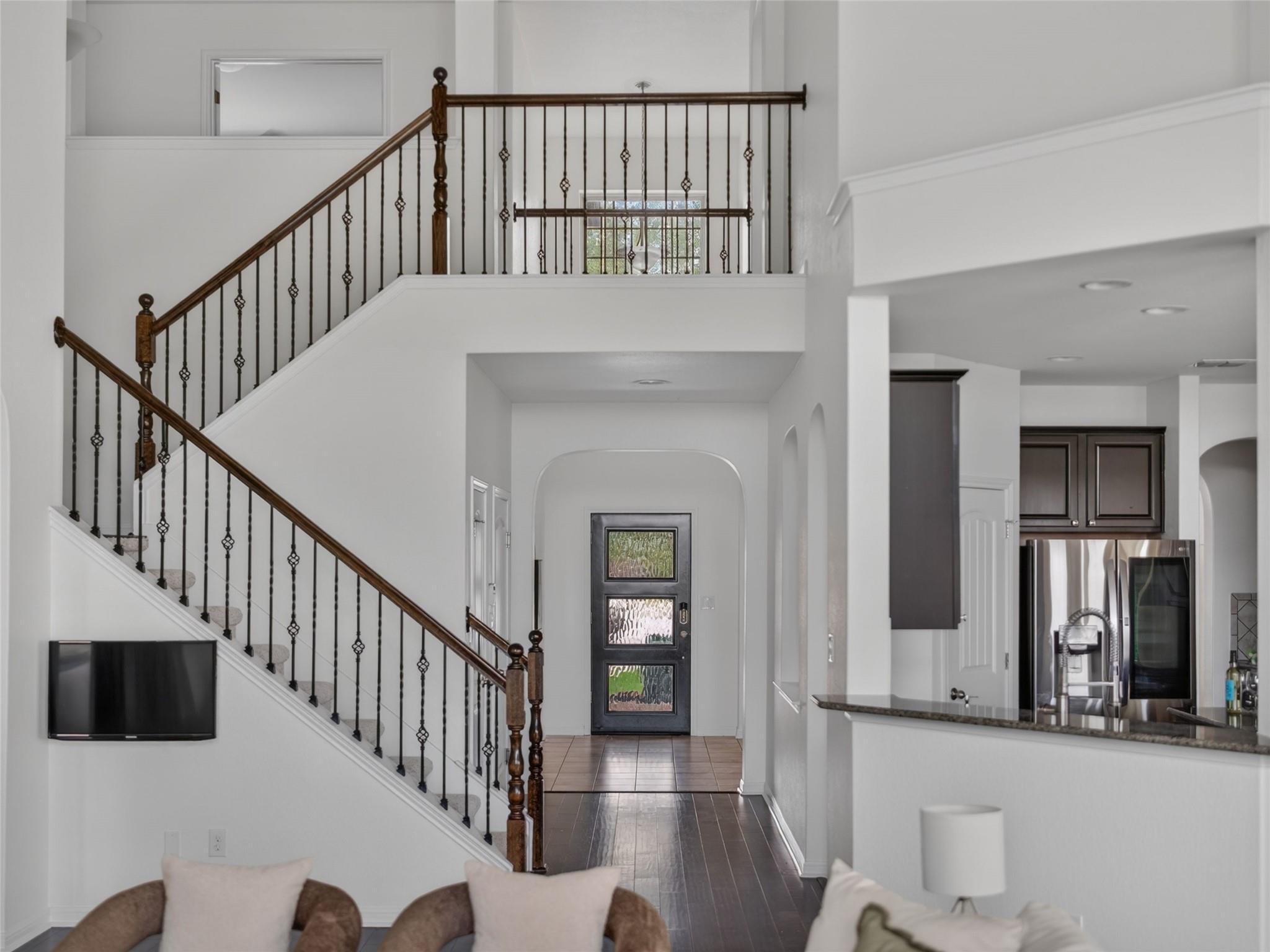Two-story entryway with a dark-railed staircase, tiled floor, and open kitchen.