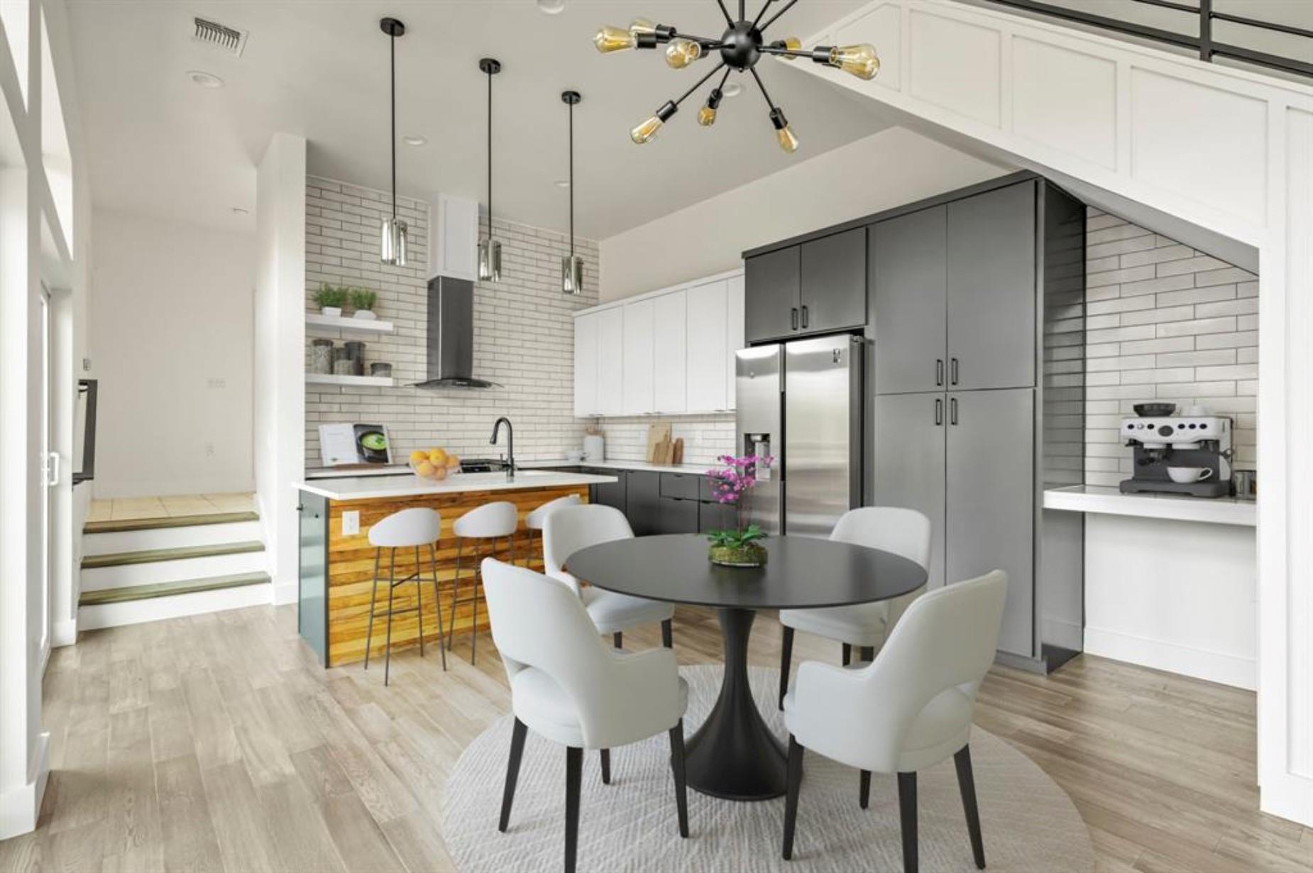 Open kitchen with gray cabinets, stainless appliances, wood-front breakfast bar, and round dining table.