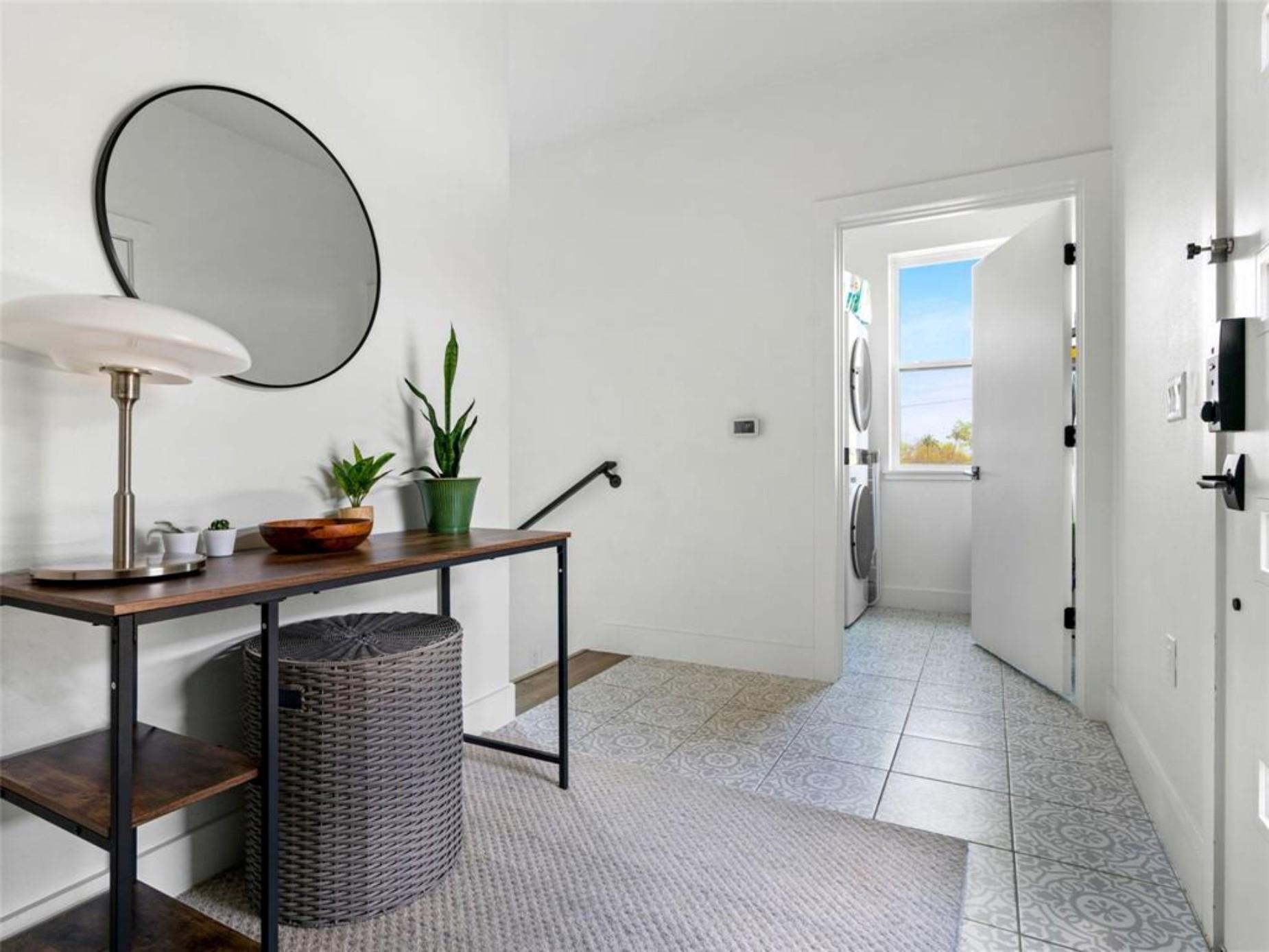 Entry hallway with a wood console and round mirror, opening onto a laundry area.