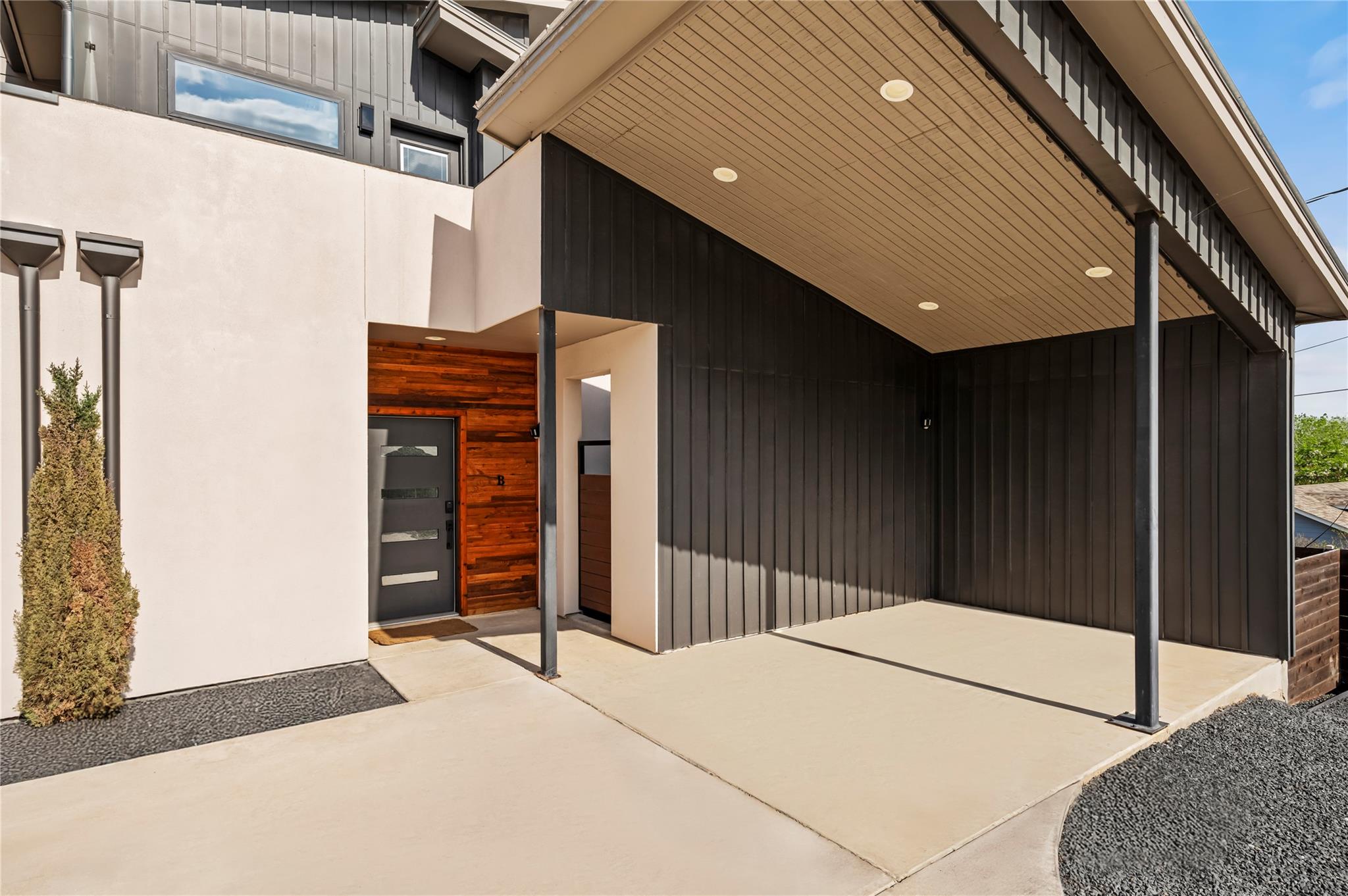 Modern home entrance with a covered concrete porch, dark siding, and wood accent wall around the front door.