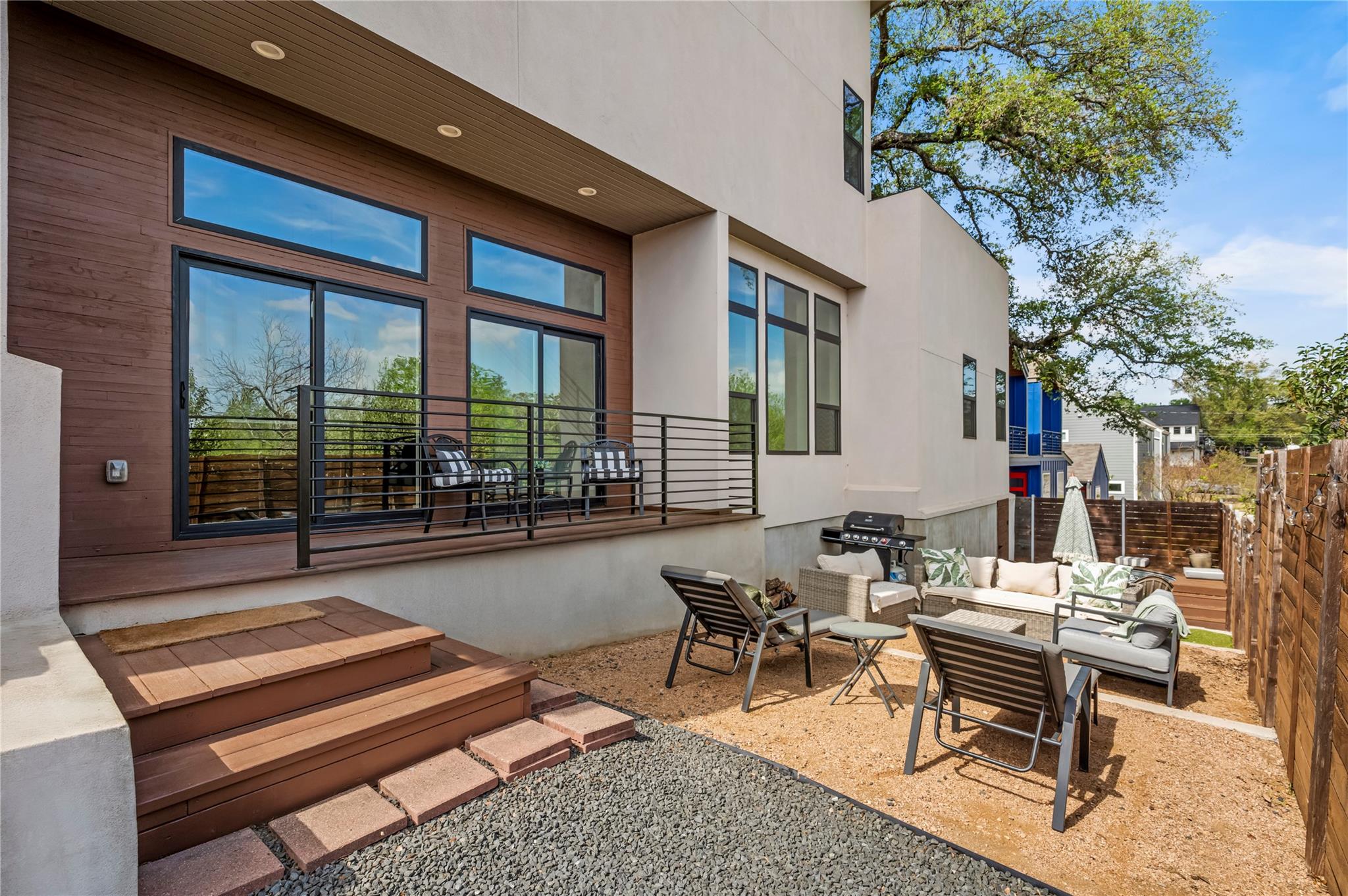Modern home with a raised wood deck overlooking a furnished patio with lounge seating and a grill.